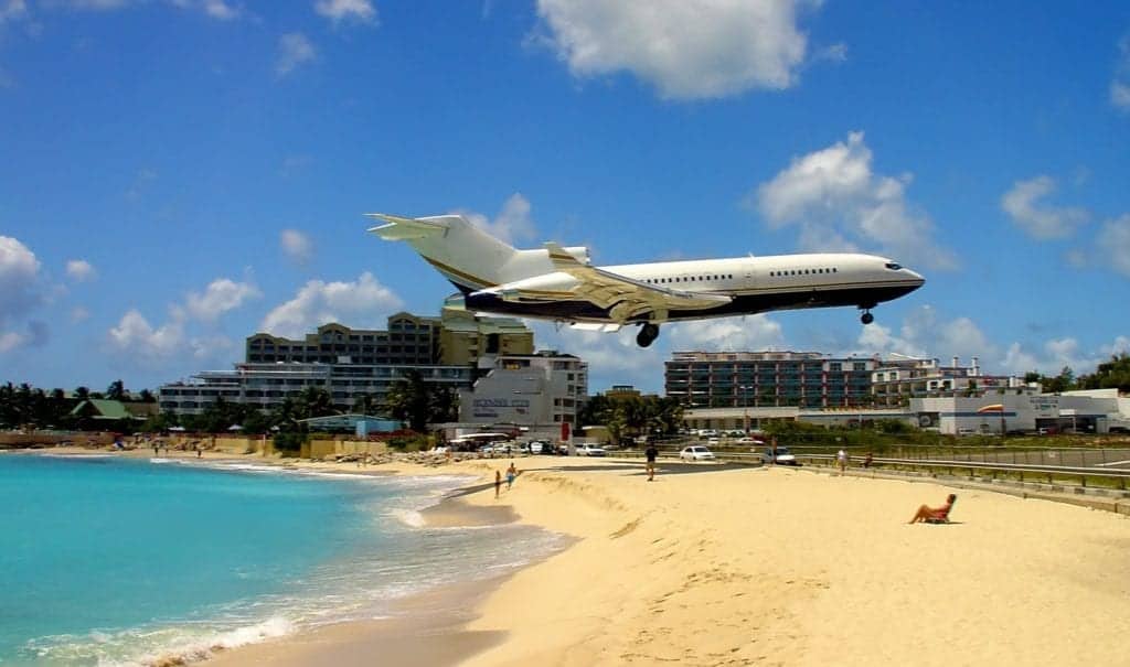 Aerial view of Maho Beach with a low-flying plane passing by, surrounded by clear blue water and sandy beach