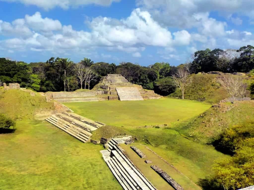 Aerial view of ancient Mayan ruins surrounded by lush greenery and clear blue skies.