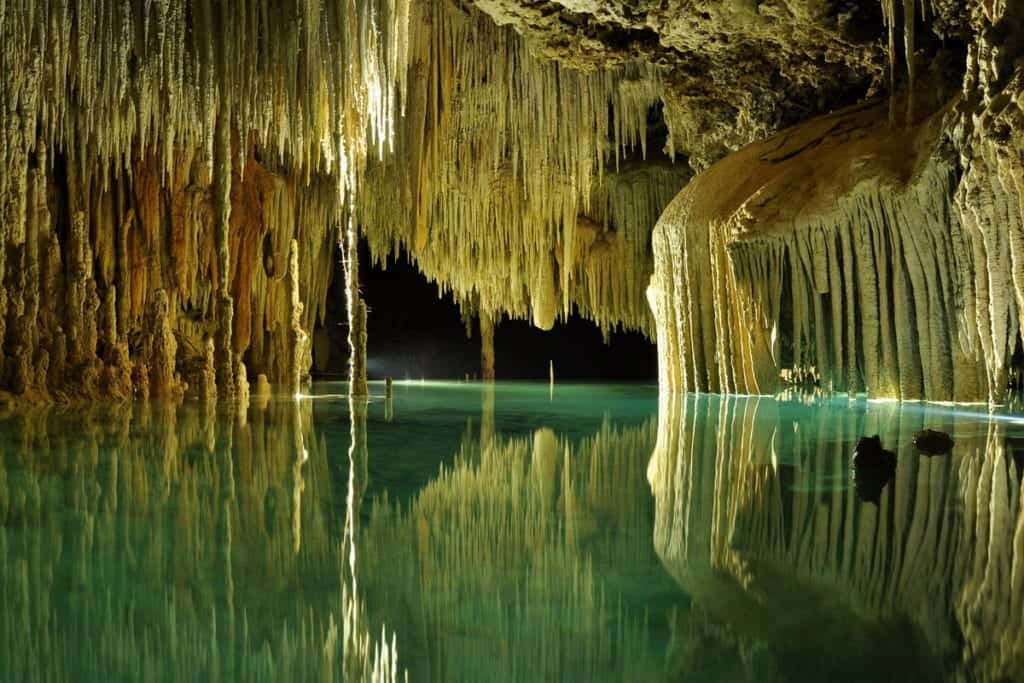 A crystal clear, underground river surrounded by cave formations and lush vegetation in the Riviera Maya, Mexico.