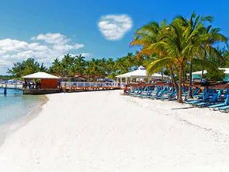 10 Best Beaches In Nassau For Cruisers 10 A vibrant scene of Blue Lagoon in Nassau, showcasing beach chairs, a white sandy beach, and coconut trees along the shore.