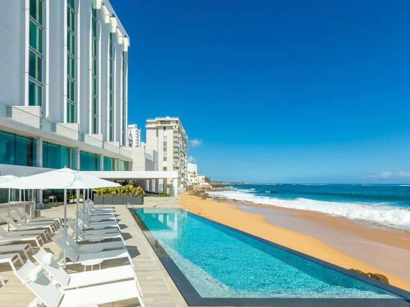 Condado Ocean Club with a clear view of its pool, the elegant building, and the expansive ocean in the background, combining luxury with scenic beauty.
