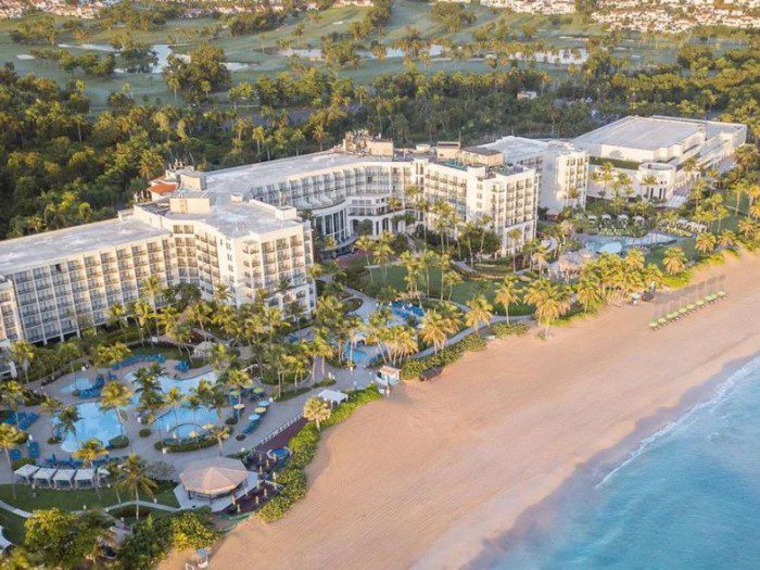 Wyndham Grand Rio Mar Golf & Beach Resort, showcases its expansive pool, the grandeur of the building complex, and the stunning ocean, highlighting the resort's luxurious and scenic setting.