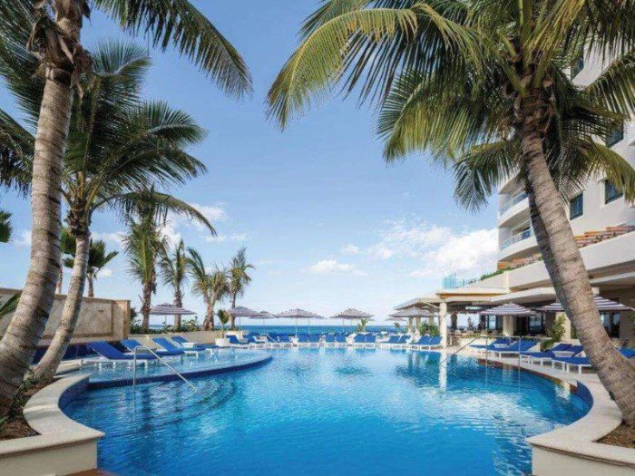 Condado Vanderbilt Hotel, highlighting its pool area surrounded by coconut trees, with a captivating view of the ocean in the background, blending tropical elegance with a breathtaking seascape.