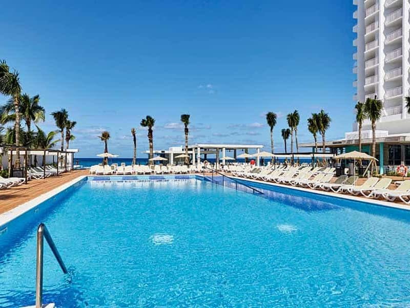 This image showcases the expansive and inviting main pool of the RIU Palace in Nassau. The pool is elegantly designed with clear, shimmering blue water that reflects the bright, sunny sky above.