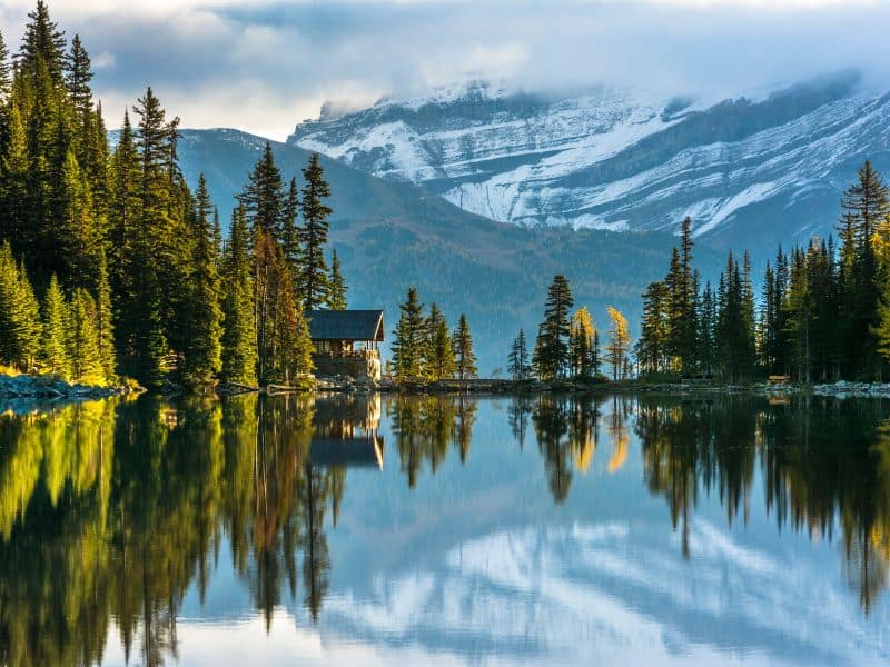 A serene and pristine view of Lake Agnes, reflecting the surrounding majestic mountains and lush greenery.