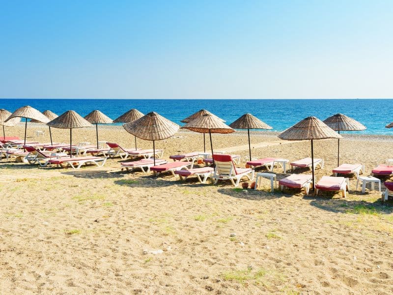 A tranquil coastal haven with golden sands, where rows of beach umbrellas provide shaded relaxation along the picturesque shores of Kusadasi, Turkey.