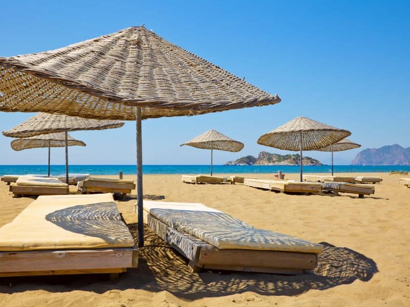 A seaside paradise where golden sands, beach umbrellas, and chairs create a perfect setting for relaxation by the turquoise waters of the Aegean Sea.
