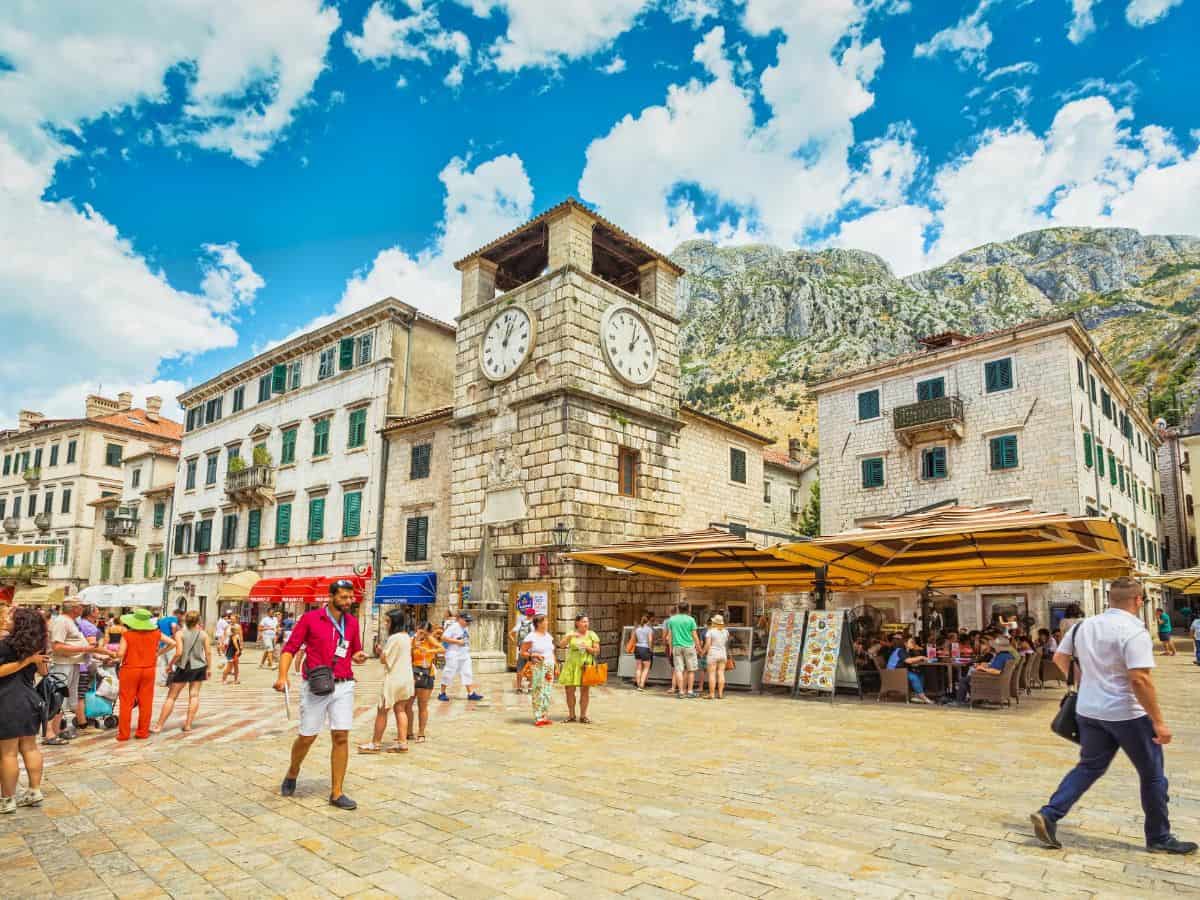 The old town of Kotor, its cobblestone streets bustling with people, framed by historic stone buildings and surrounded by ancient walls.