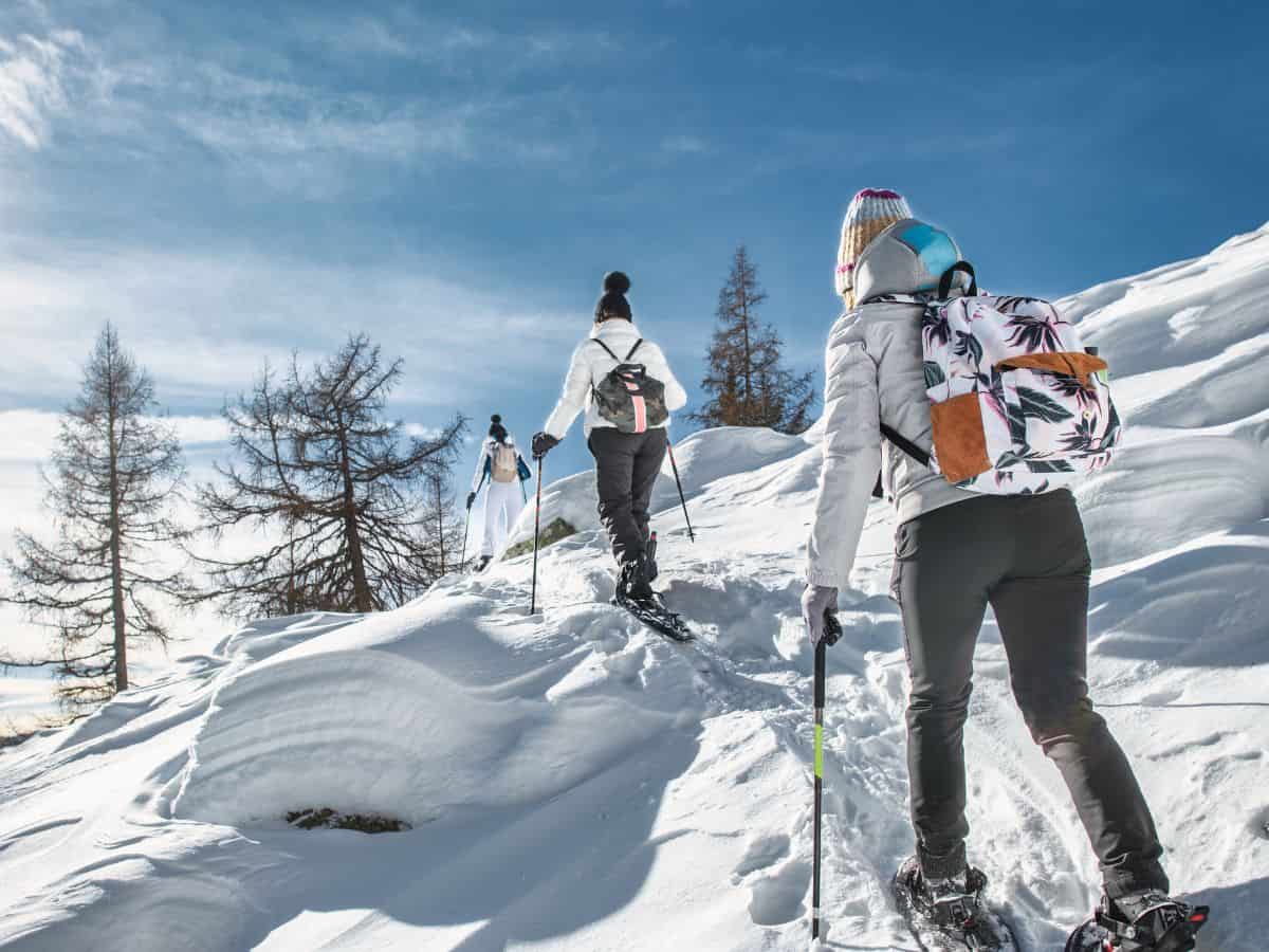 Three individuals clad in winter attire, exploring a snow-covered landscape adorned with their snowshoes, casting shadows on the pristine white surface.