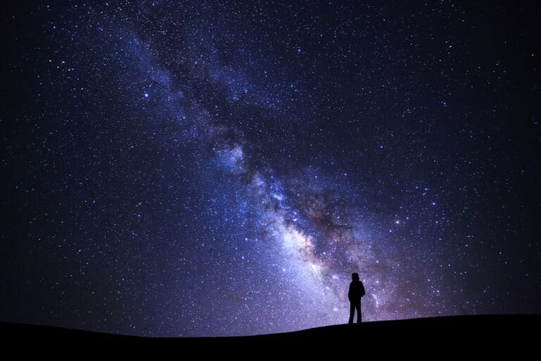 A solitary figure stands atop a dune against a backdrop of the Milky Way's cosmic splendor in Joshua Tree National Park