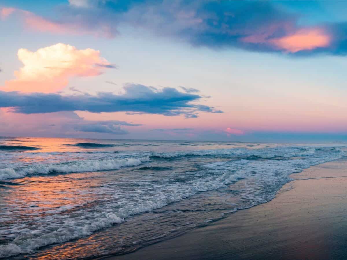 A pastel-hued sunset at Myrtle Beach, with soft waves lapping the shore and a dynamic sky filled with clouds reflecting the sun's fading light.