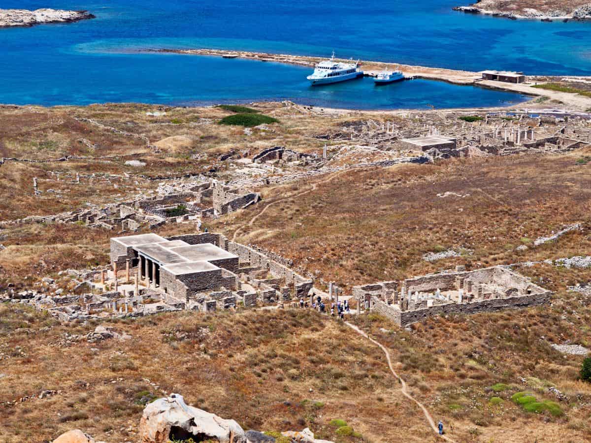 An overview of the Island of Delos, Greece, showcasing ancient ruins, historical sites, and a rugged landscape against the backdrop of the Aegean Sea.