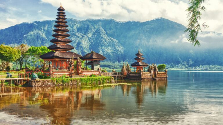 Traditional temple on the shore of a serene lake with mountain backdrop in Bali.
