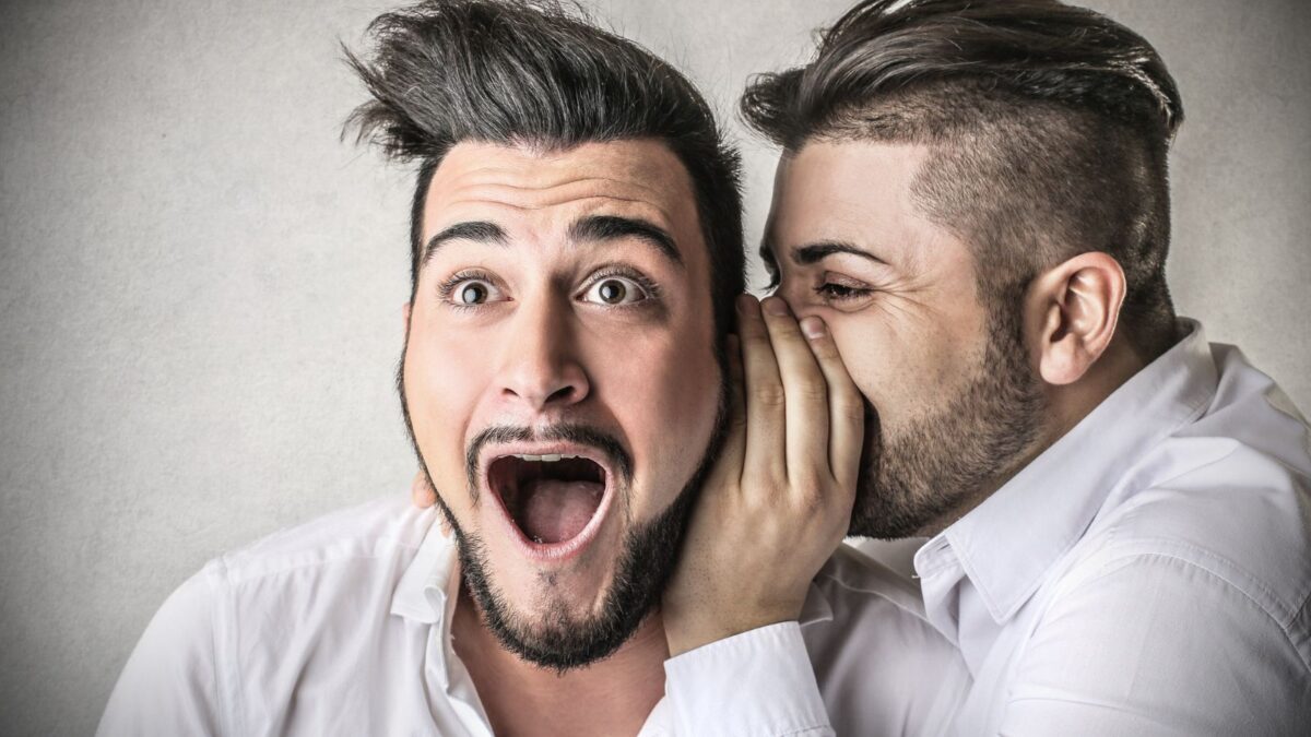 A man whispering into another man's ear, while the man getting the information seems surprised.