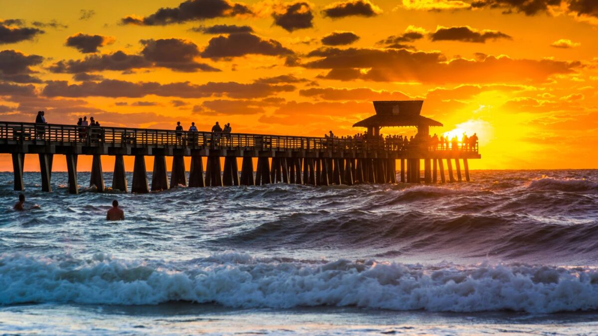 Yellow and orange sunset over pier in Naples Fl with waves crashing and a cloudy sky