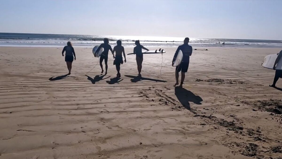 A group of surfers with boards walking on a sandy beach towards the ocean waves.