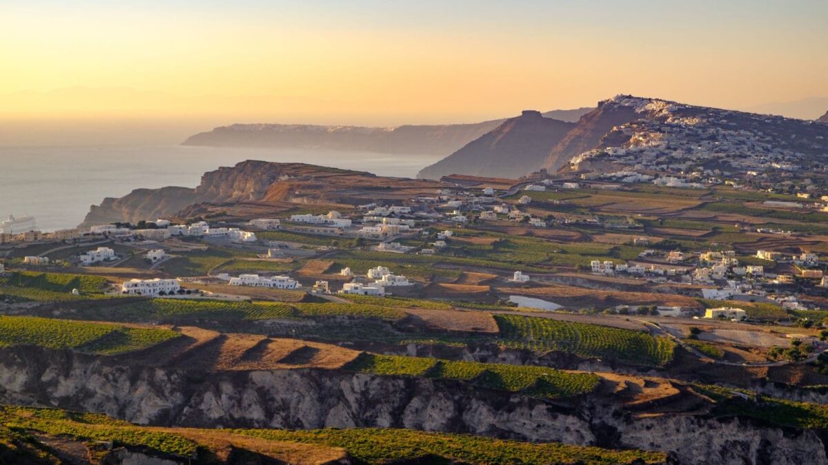 erial view of a picturesque Santorini vineyard, showcasing the unique landscape and terraced vineyards typical of Santorini wineries, under a clear blue sky.
