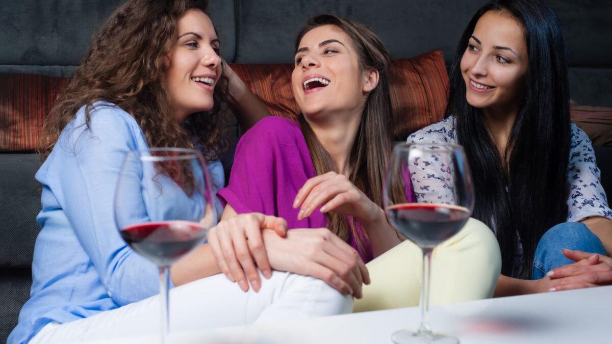 A cozy gathering of three women enjoying a conversation and a glass of red wine, sitting comfortably on a sofa, sharing a moment of camaraderie and relaxation.