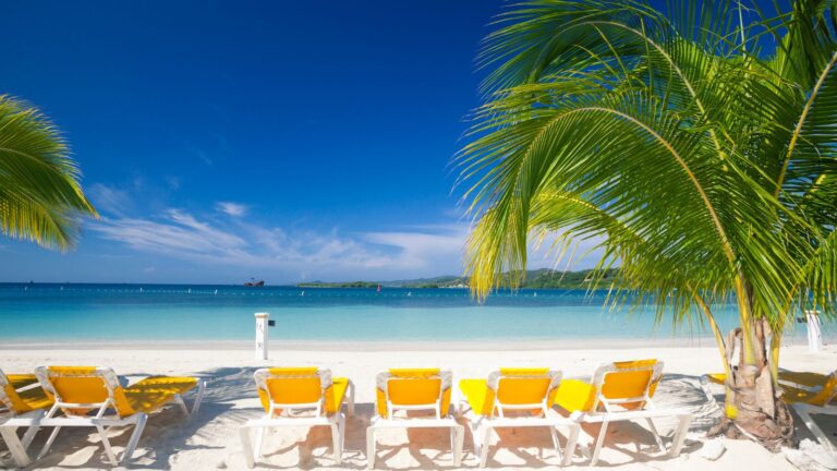 Tropical beach view with yellow lounge chairs and palm trees. In one of the best Roatan Hundoras Beaches.