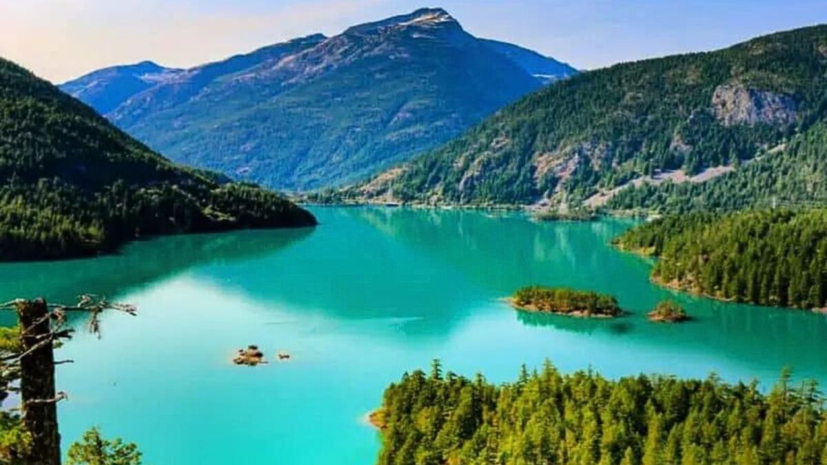 20 Breathtaking Lakes That Are True Natural Wonders! 3 The image depicts Diablo Lake, known for its striking turquoise-colored water, nestled in a valley surrounded by lush evergreen forests and rugged mountain peaks. The lake appears calm and is dotted with small islands, enhancing its scenic beauty. The surrounding mountains have some patches of snow, indicating either high altitude or a colder season