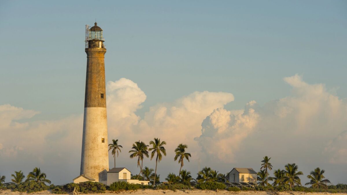 The Cheapest Way To Get To Dry Tortugas National Park 14 Lighthouse with palm trees at sunset with large clouds in the background.