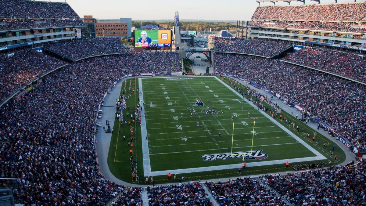 10 Iconic Football Stadiums Every Fan Should Experience 10 A bustling Gillette Stadium during a game, filled with fans. The view showcases the multiple levels of stands, the field of play in the center, and a large screen displaying a player. The stadium appears as a hub of activity and excitement.