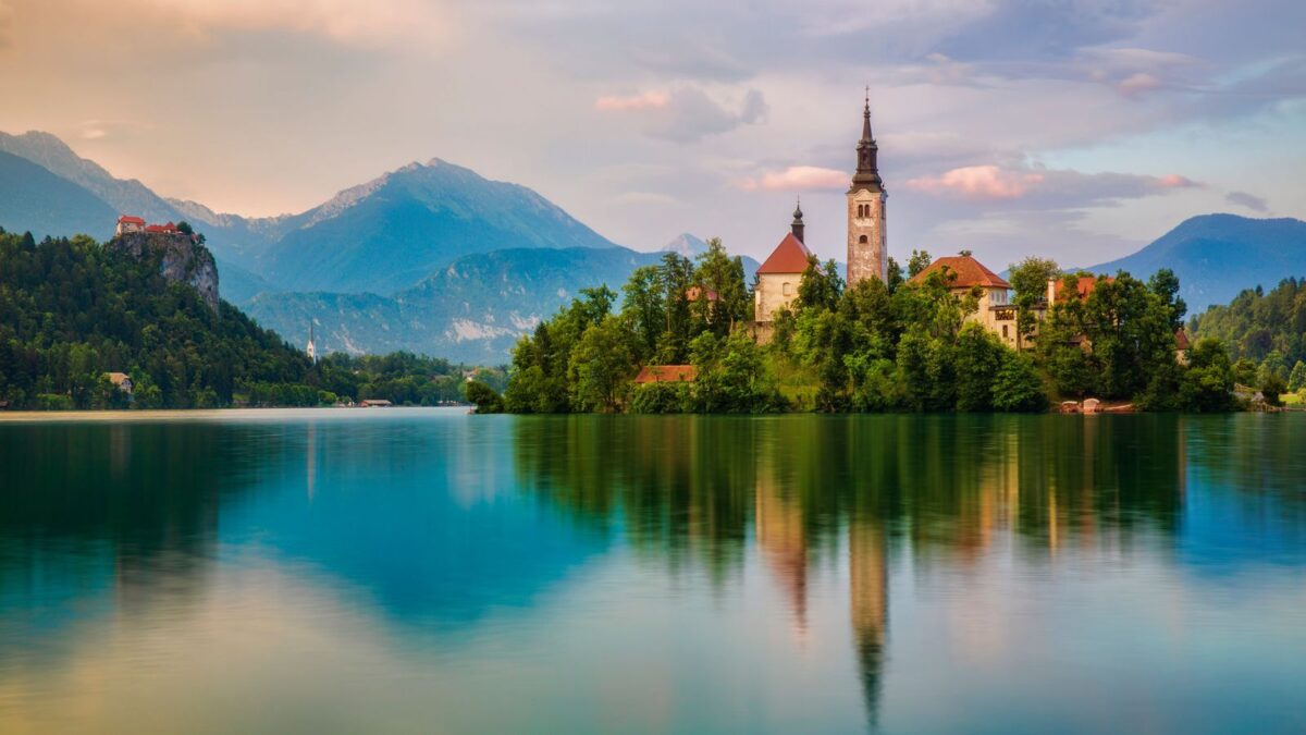 20 Breathtaking Lakes That Are True Natural Wonders! 4 The tranquil waters of Lake Bled at twilight, with the island church and castle against a backdrop of soft clouds and forested hills.