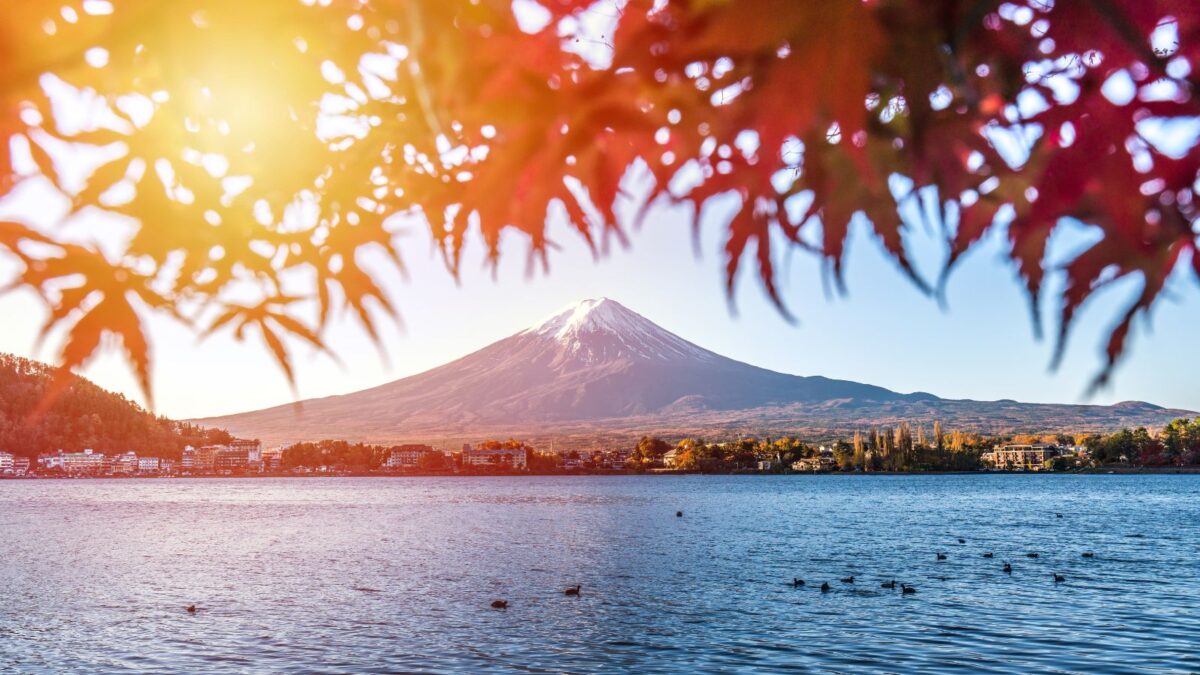 20 Breathtaking Lakes That Are True Natural Wonders! 15 A serene view of Mount Fuji with a foreground of autumn leaves framing the tranquil lake waters and the lakeside town.
