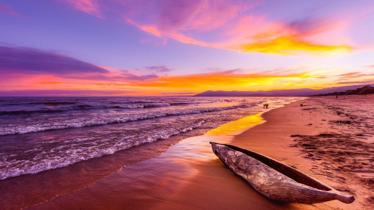 20 Breathtaking Lakes That Are True Natural Wonders! 19 Sunset at a beach, with vibrant purple and orange hues in the sky reflected on the shoreline, and a driftwood log in the foreground.