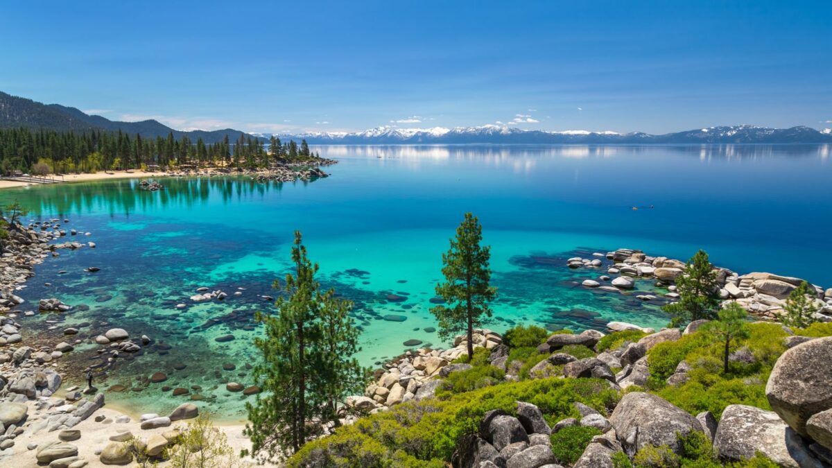 20 Breathtaking Lakes That Are True Natural Wonders! 5 The crystal-clear blue waters of Lake Tahoe, lined with pine trees and smooth boulders, with snow-covered mountains in the distance.