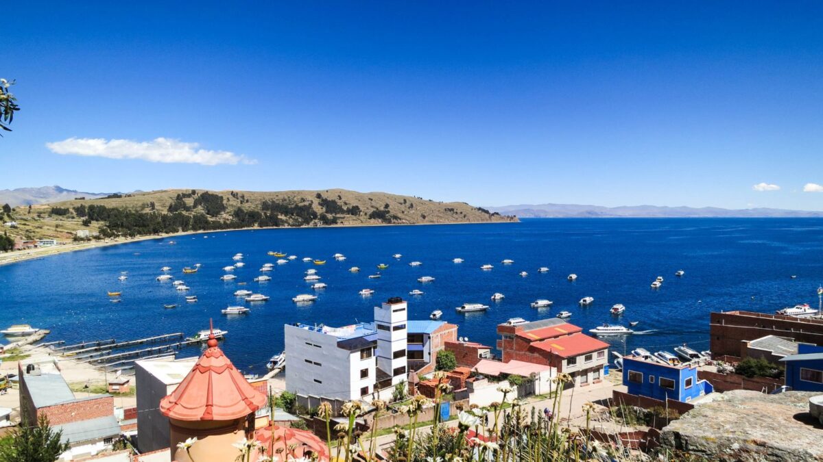 20 Breathtaking Lakes That Are True Natural Wonders! 14 A view from the town onto the vast blue expanse of Lake Titicaca dotted with boats under a clear sky.