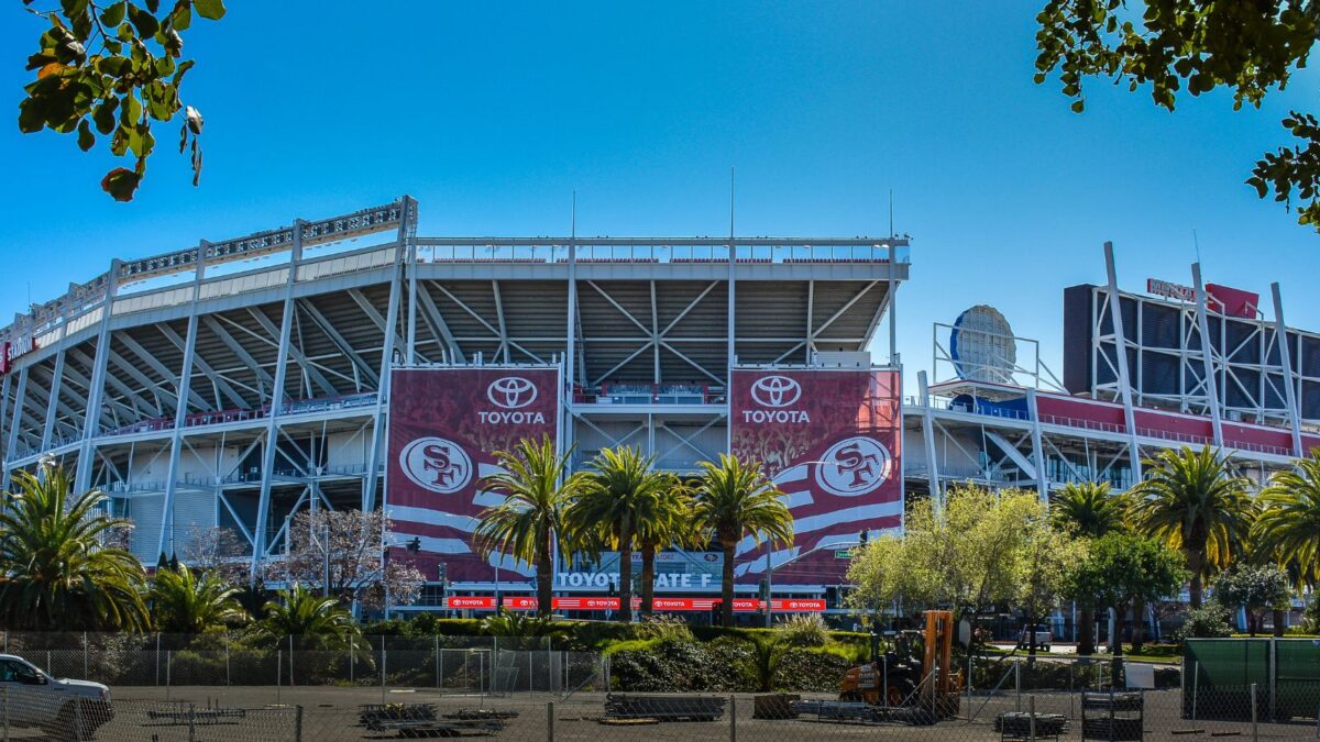 10 Iconic Football Stadiums Every Fan Should Experience 8 The exterior of Levi's Stadium, home of the San Francisco 49ers, with large banners featuring the team's branding. The stadium's open-air design and steel structures are visible, with a clear blue sky in the background.