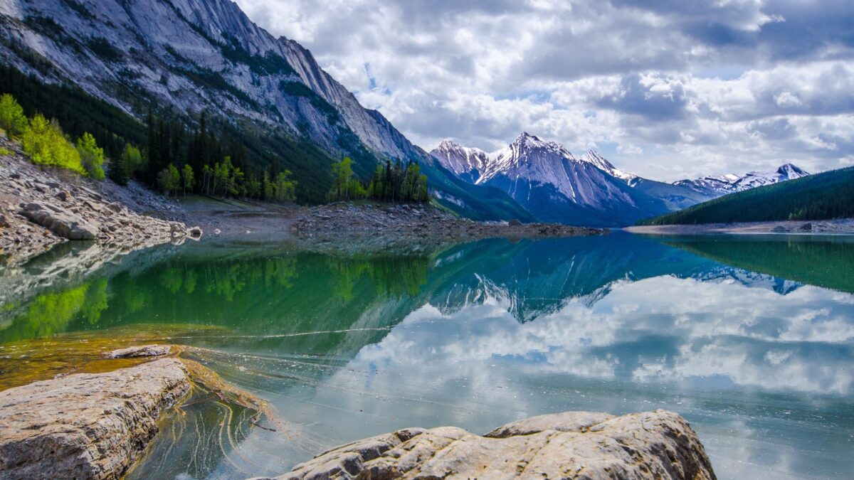 20 Breathtaking Lakes That Are True Natural Wonders! 16 The placid waters of Maligne Lake reflect the surrounding rugged mountains and evergreen forests under a cloudy sky.