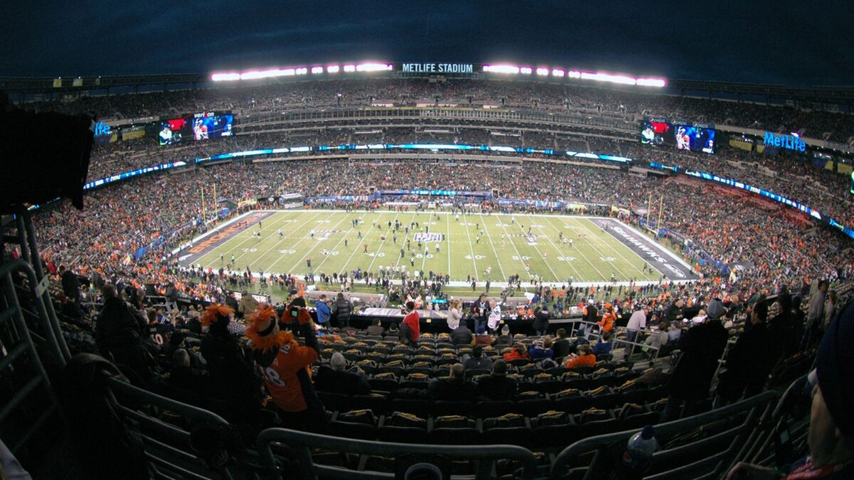 10 Iconic Football Stadiums Every Fan Should Experience 7 MetLife Stadium during a night game, the stands glowing with lights and filled with fans. The stadium's round shape and multiple tiers are illuminated, emphasizing the live game experience.
