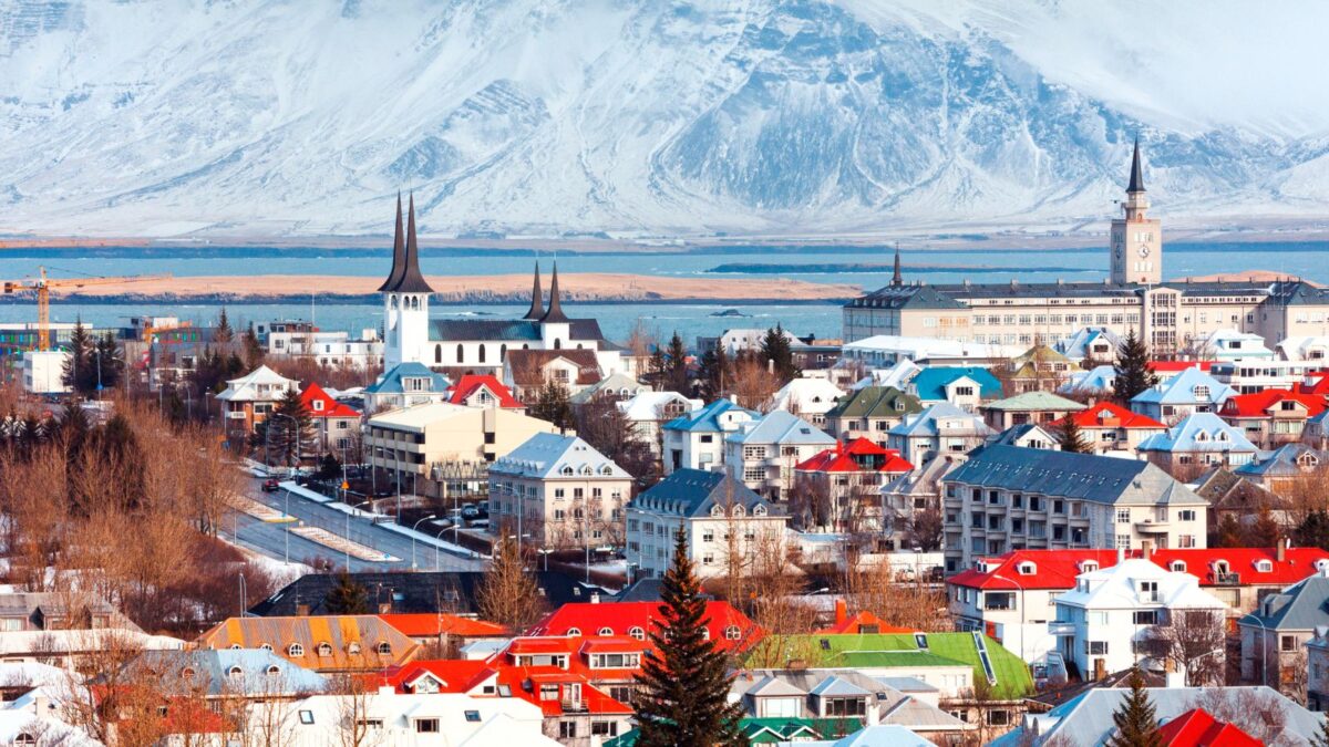 Scenic view of Reykjavik with colorful buildings, church spires, and snow-capped mountains in the background.