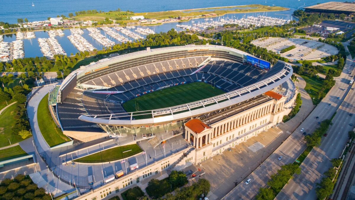 10 Iconic Football Stadiums Every Fan Should Experience 3 Soldier Field overlooking a marina, with its classical columns juxtaposed with modern stadium design. The vast stands and playing field are seen from above, with the city and water providing a scenic backdrop.