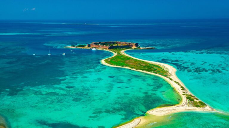 Aerial view of a historic fortress on an island with a connecting sandbar and turquoise sea.