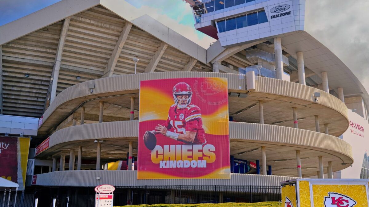 10 Iconic Football Stadiums Every Fan Should Experience 6 A view of Arrowhead Stadium's exterior with a large banner of a Kansas City Chiefs player, and the words "Chiefs Kingdom" prominently displayed. The stadium's multi-tiered ramps and concrete structure are visible under a bright sky.