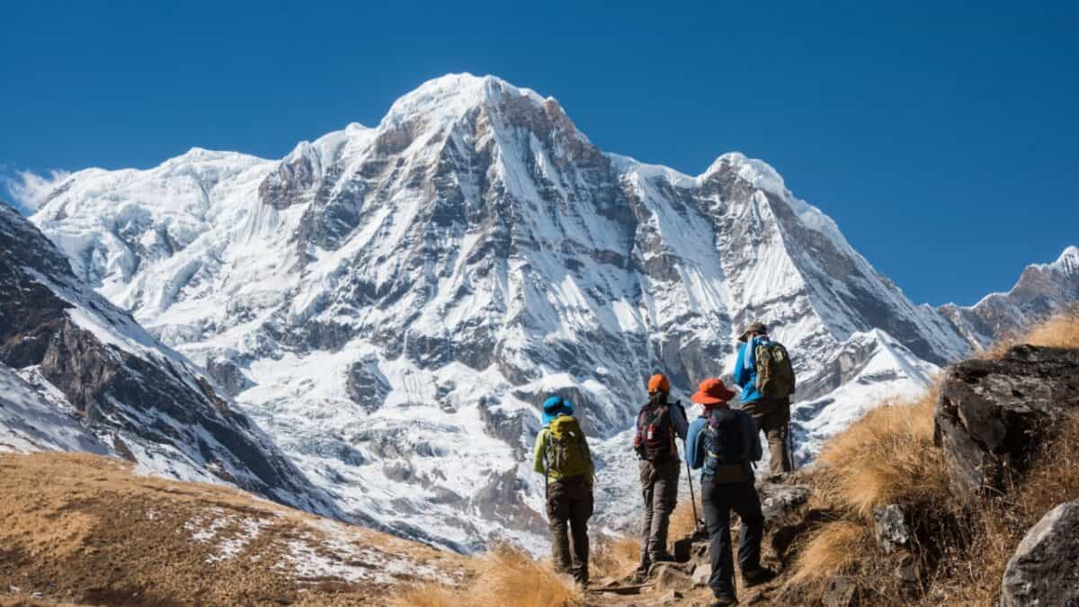 A group of hikers with backpacks trekking towards a majestic snow-capped mountain under a clear blue sky.