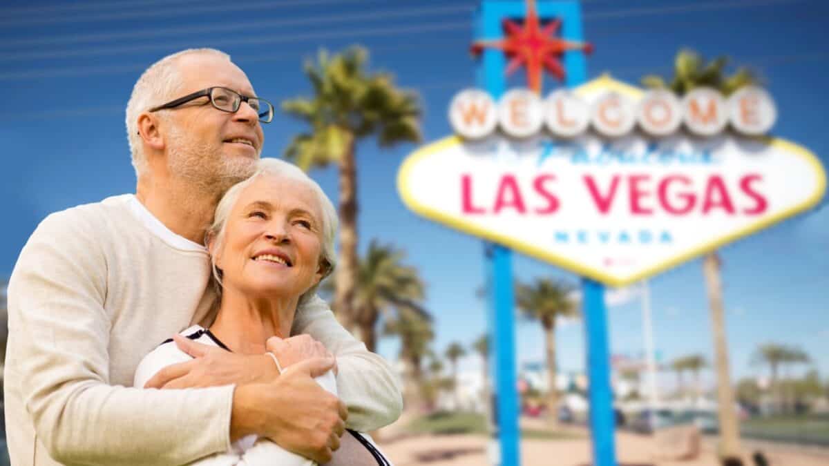 A senior couple embracing with smiles on their faces, standing in front of the iconic "welcome to fabulous las vegas" sign, enjoying their vacation in the vibrant city.