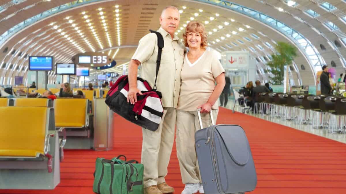 Senior couple smiling with luggage at the airport, ready to embark on a vacation adventure.