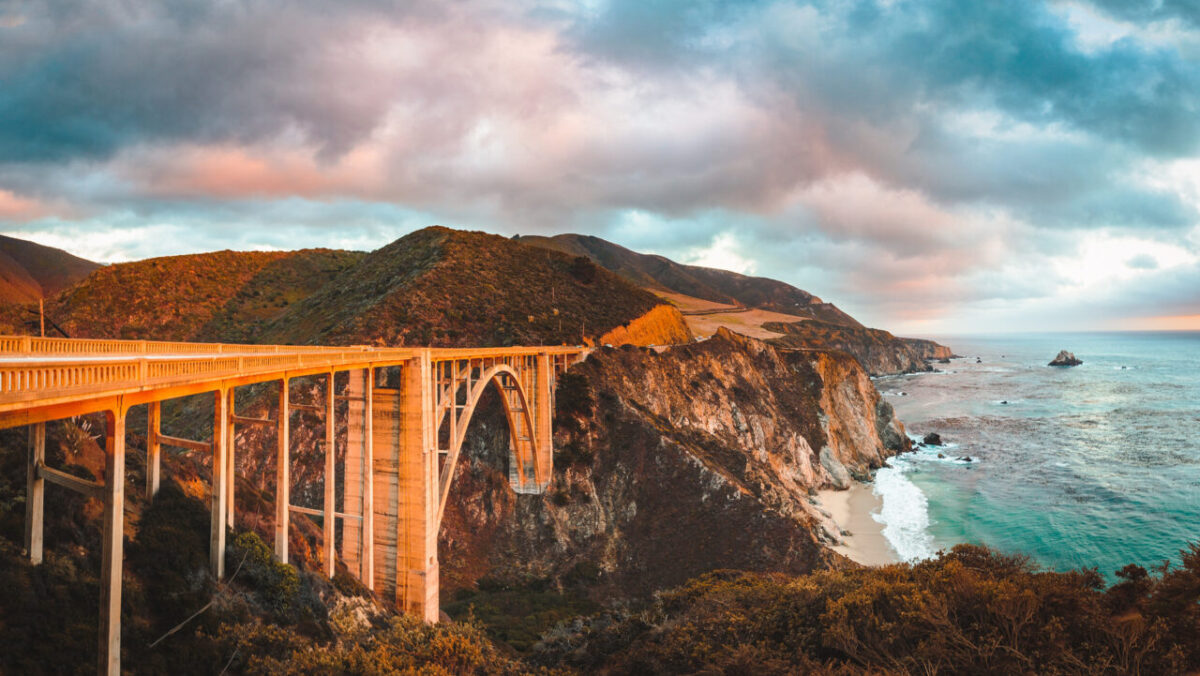 6 U.S. Budget-Friendly Road Trips Better Than Luxury Vacations 9 Scenic panoramic view of historic Bixby Creek Bridge along world famous Highway 1 in beautiful golden evening light at sunset with dramatic cloudscape in summer, Monterey County, California, USA