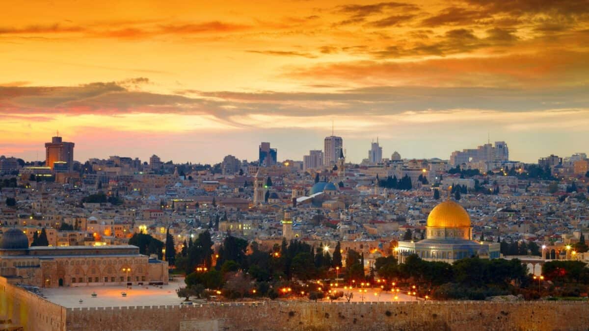 
A panoramic view of Jerusalem at sunset, with the Dome of the Rock in the foreground and the city skyline in the background.