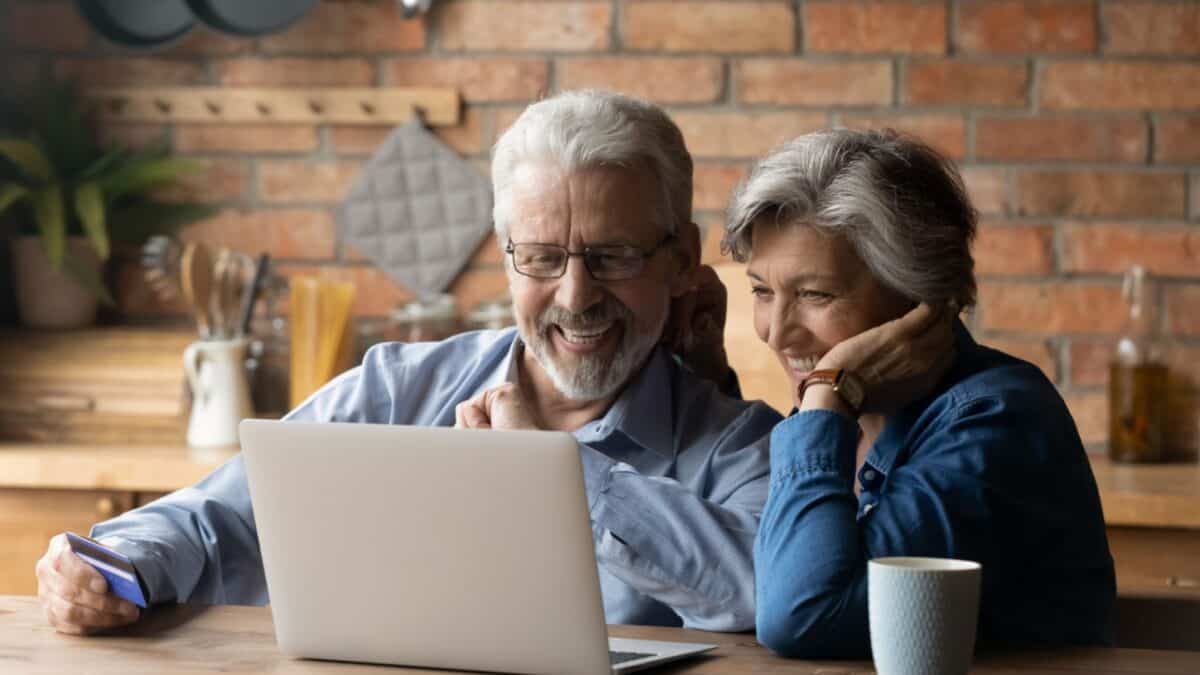 A cheerful senior couple enjoying a moment together as they look at a laptop screen in a cozy home environment.