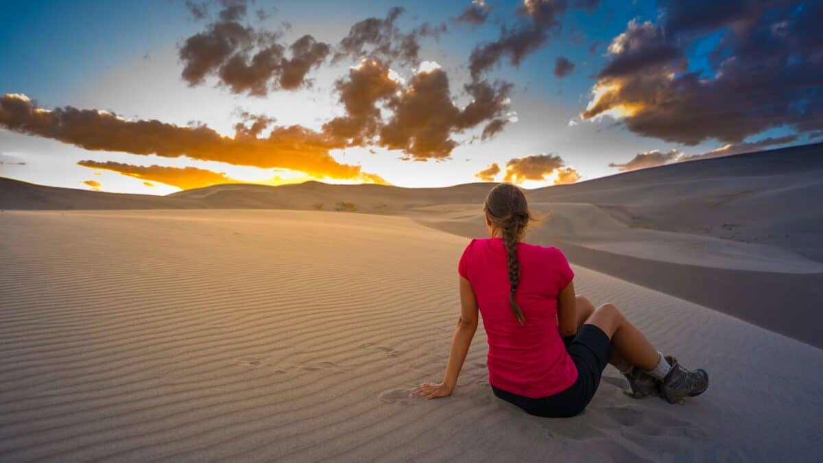 Person in a pink shirt sitting on a sand dune watching the sunset.