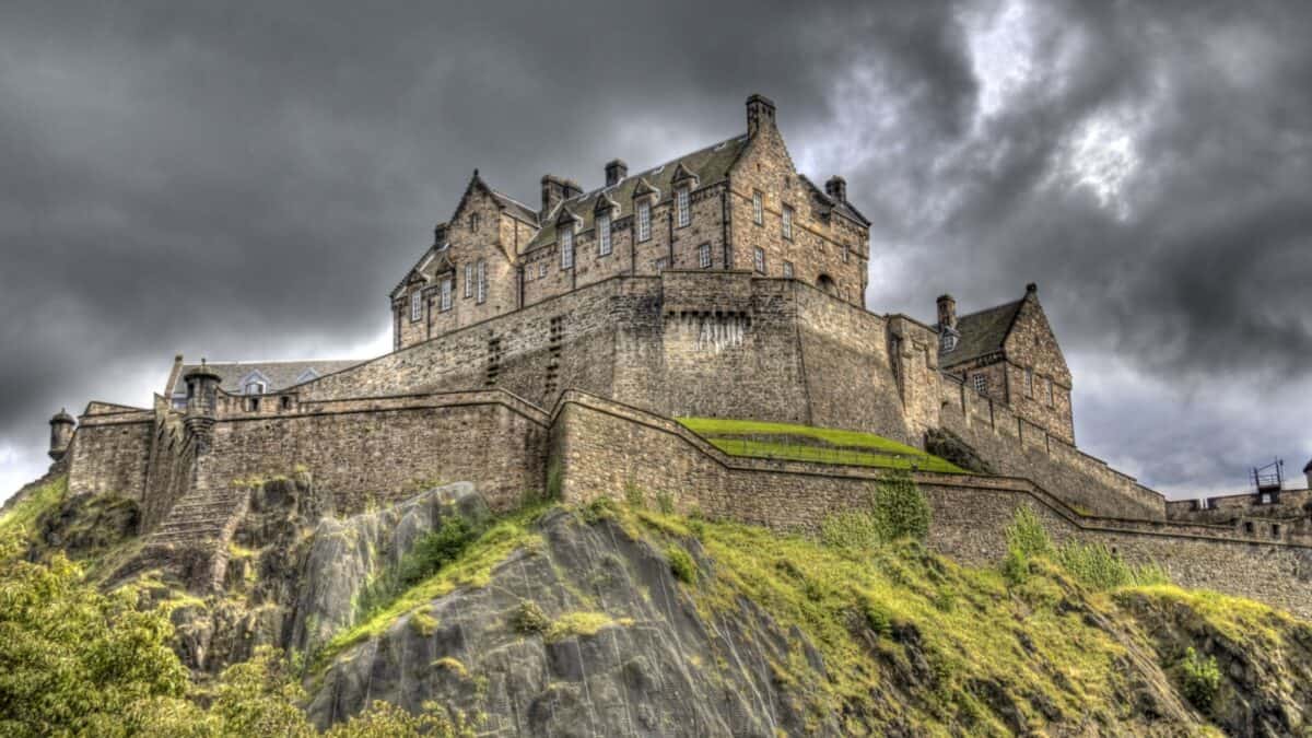 A grand castle with turreted towers sitting atop a steep hill, under a dramatic, stormy sky.