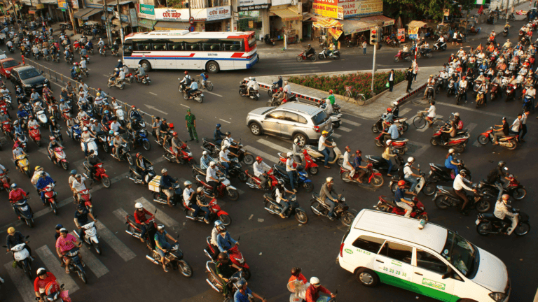 Busy urban intersection teeming with a multitude of motorcycles weaving around cars and buses during peak traffic hours.