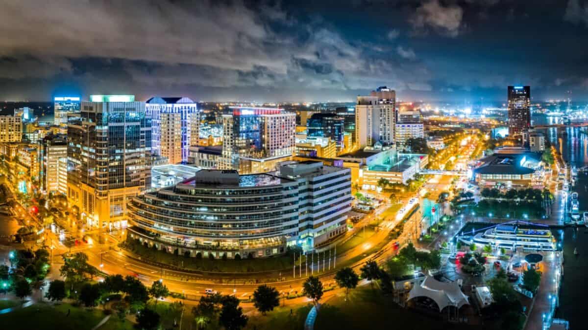 A panoramic night view of a bustling metropolis, showing illuminated streets and skyscrapers under a dramatic cloudy sky.