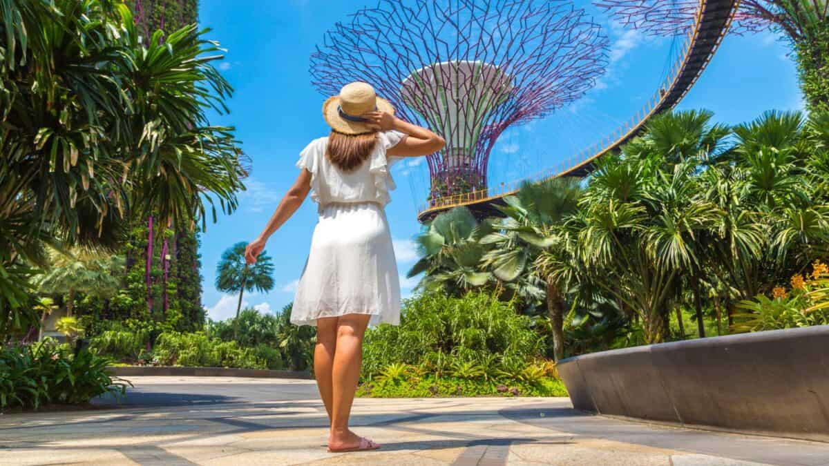 20 Best Places For Solo Female Travelers 22 A woman in a white dress and straw hat is walking towards the tall tree-like structures at gardens by the bay in singapore on a sunny day.