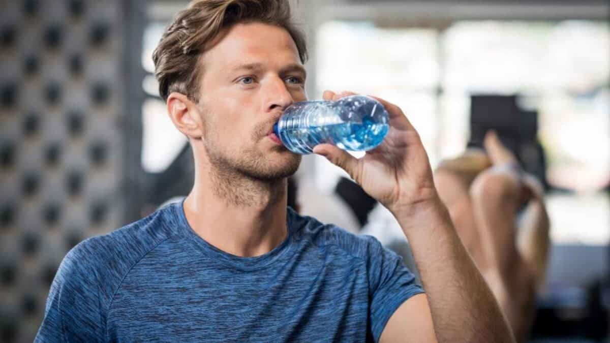 Man in a blue shirt drinking water from a bottle at the gym.